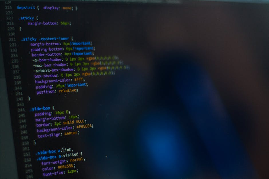 The image displays a computer screen with lines of code in various colors, including red, green, blue, and purple, against a predominantly black background. The code appears to be HTML or CSS, with vi